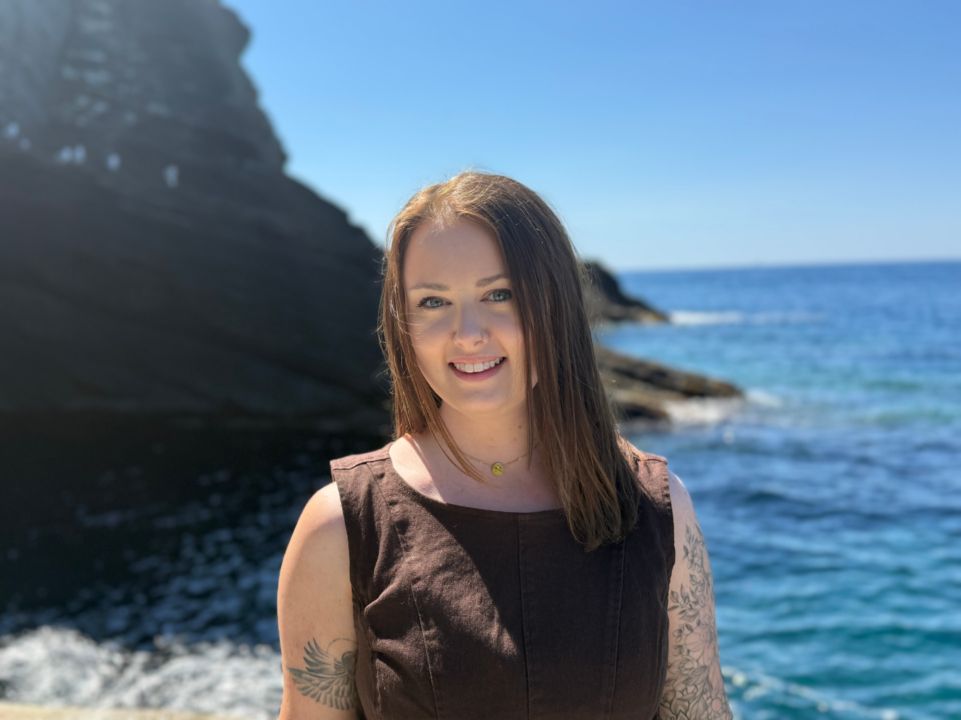 Emma Bostian smiling on a rocky coastline with the sea behind her